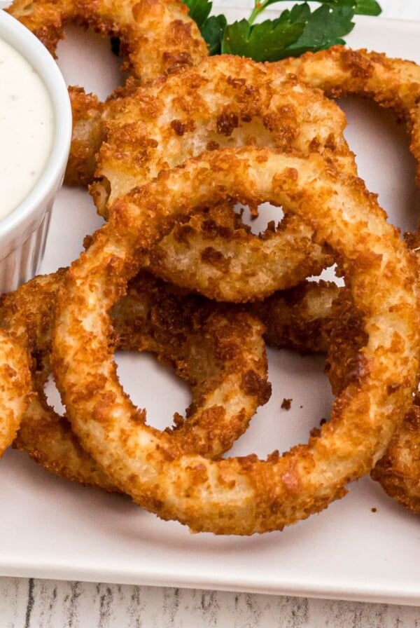 Golden crispy onion rings on a white plate served with ranch dressing.