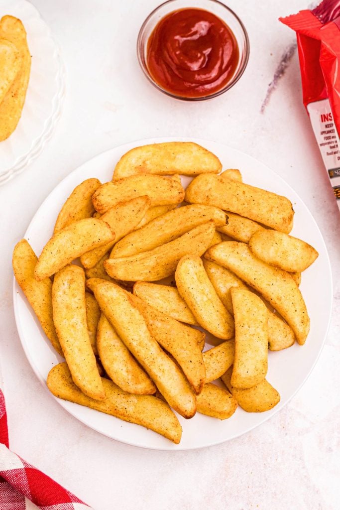 Golden seasoned crispy Red Robin steak fries on a white plate served with a small bowl of ketchup. 