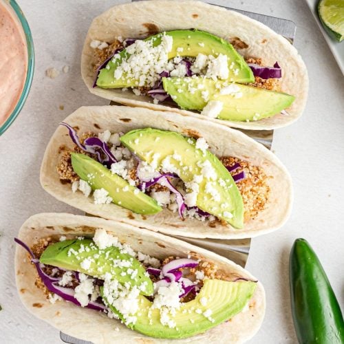 Battered cooked fish pieces in a flour tortilla tipped with avocado, cabbage and cheese.