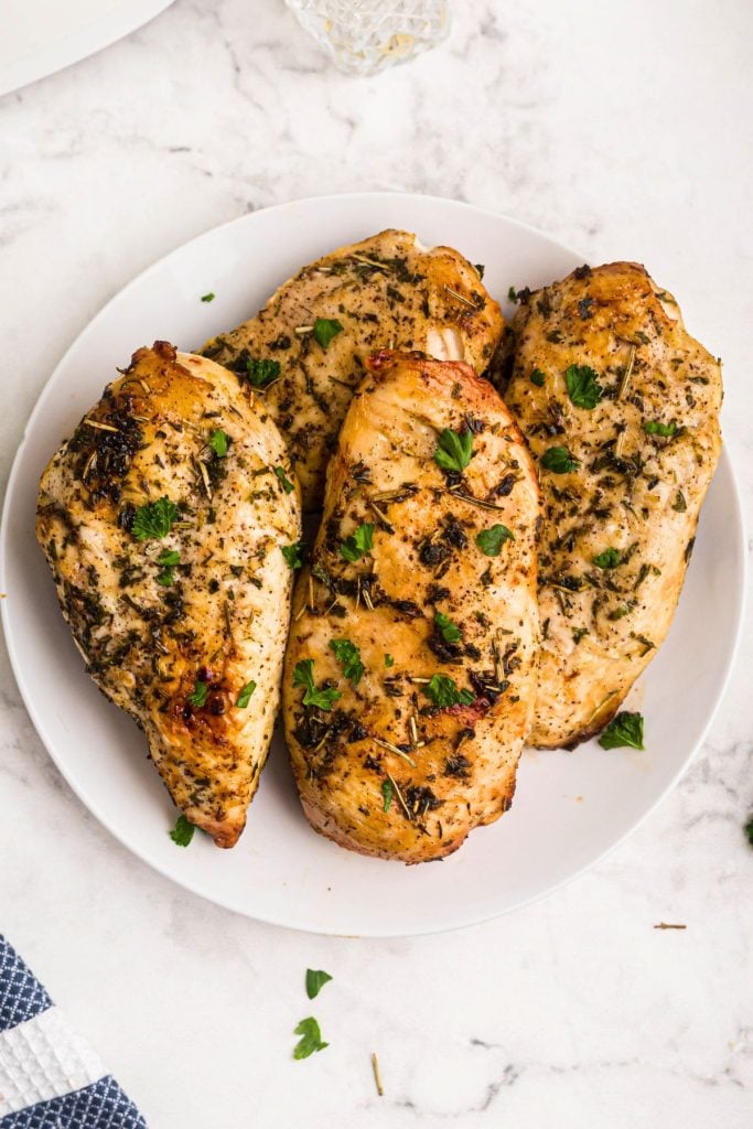 Golden juicy seasoned chicken breasts on a white plate on a marble table. 