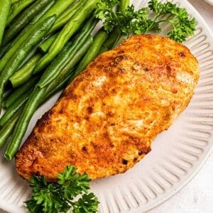 Golden, air fried chicken on a white plate with green beans.