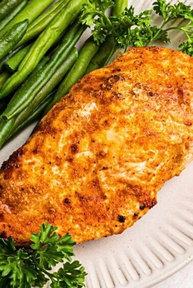 Golden, air fried chicken on a white plate with green beans.