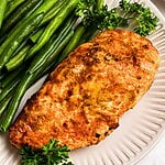 Golden, air fried chicken on a white plate with green beans.