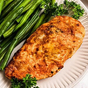 Golden, air fried chicken on a white plate with green beans.