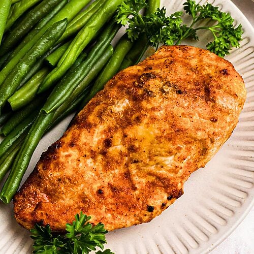 Golden, air fried chicken on a white plate with green beans.