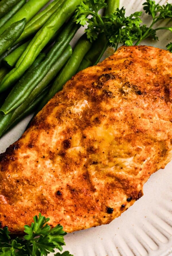 Golden, air fried chicken on a white plate with green beans.