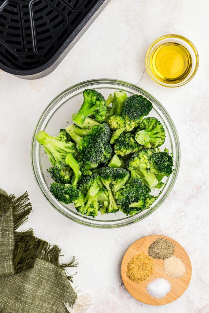 Frozen broccoli with olive oil and seasonings on a white marble table. 
