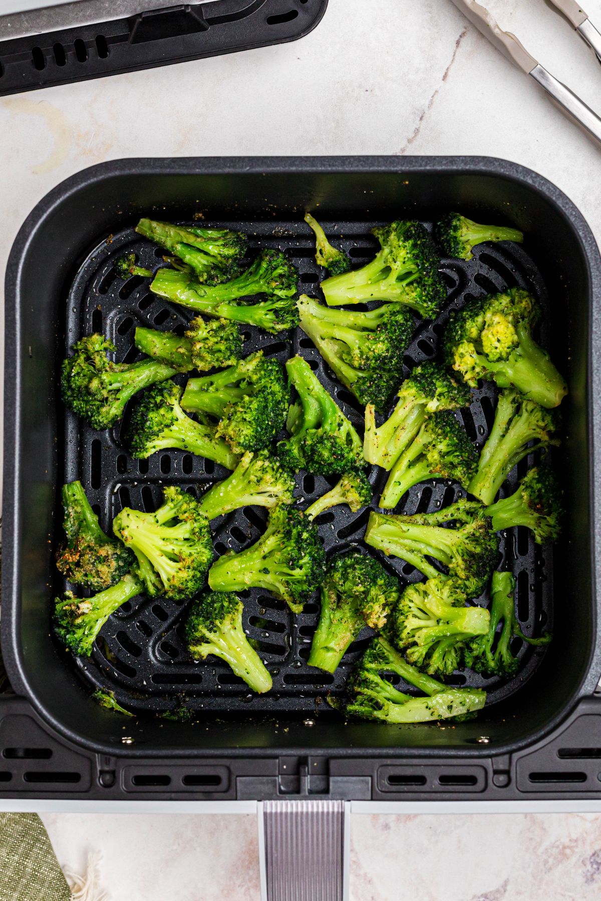 Seasoned broccoli in the air fryer basket after being cooked.