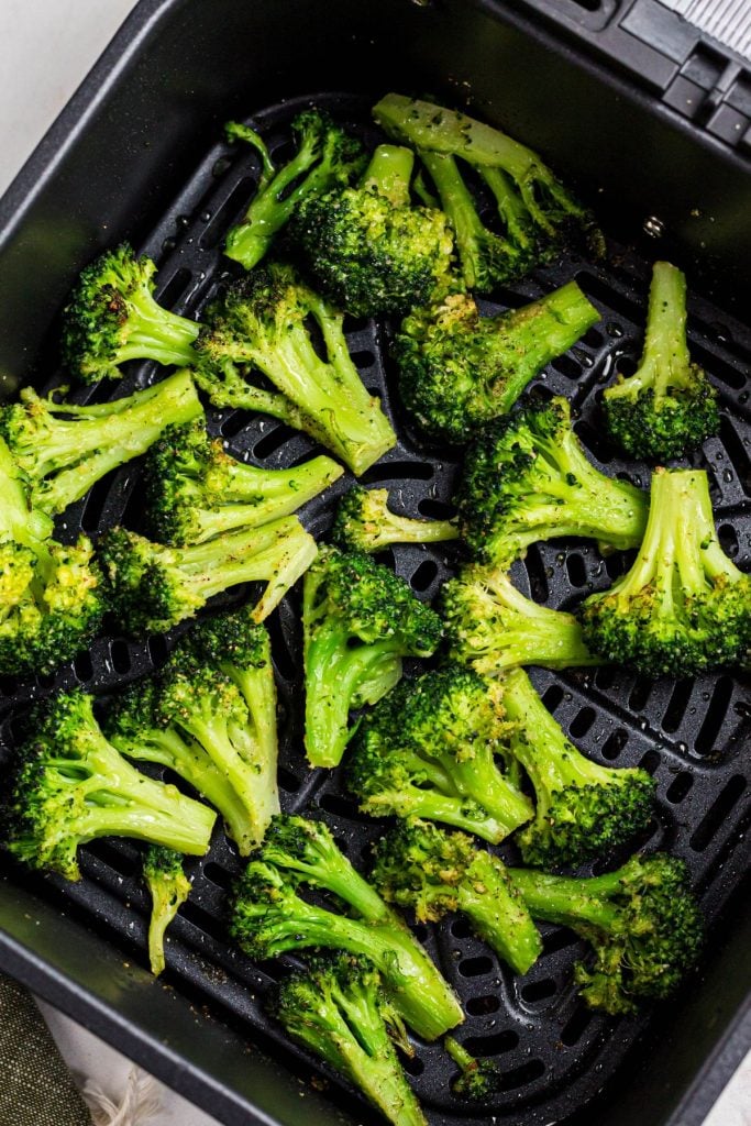 Green seasoned broccoli in the air fryer basket after being cooked. 