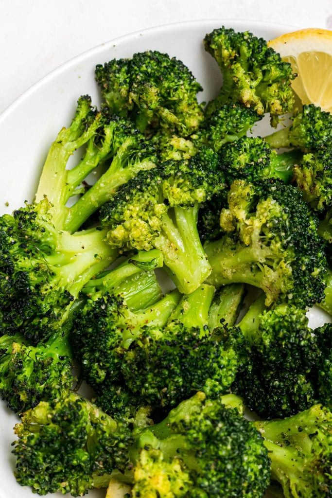 Green juicy broccoli on a white plate with a lemon wedge. 