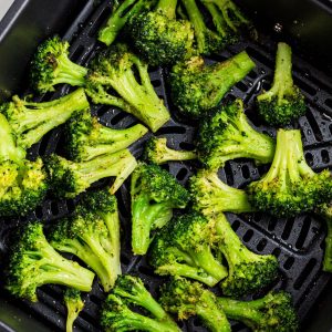 Seasoned broccoli in the air fryer basket after being cooked.