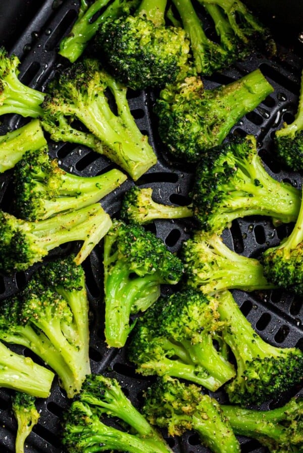 Seasoned broccoli in the air fryer basket after being cooked.