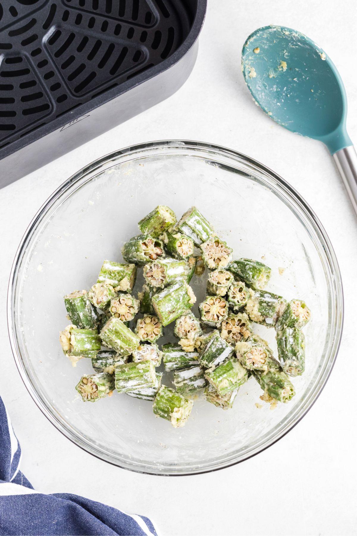 Fresh okra cut into pieces, tossed in a clear glass bowl with cornstarch, garlic, and seasonings.