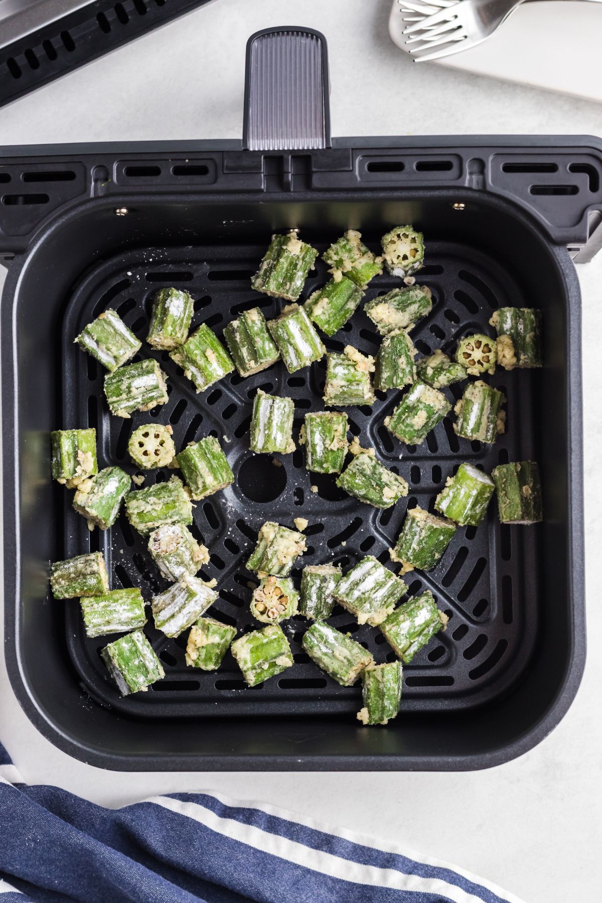 Coated okra pieces in an air fryer basket before being cooked.