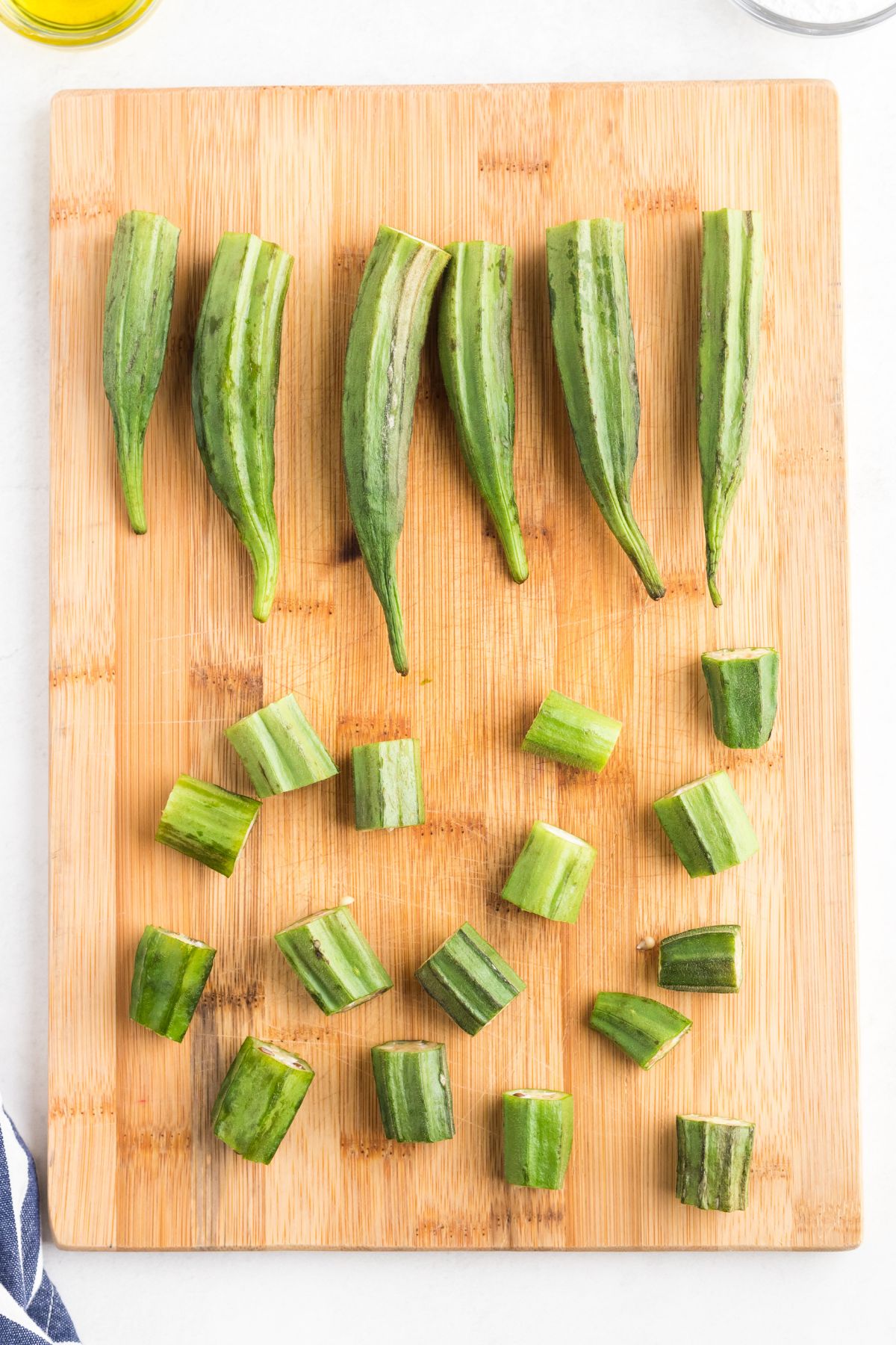 Fresh uncooked okra on a wooden cutting board with stems cut and removed.