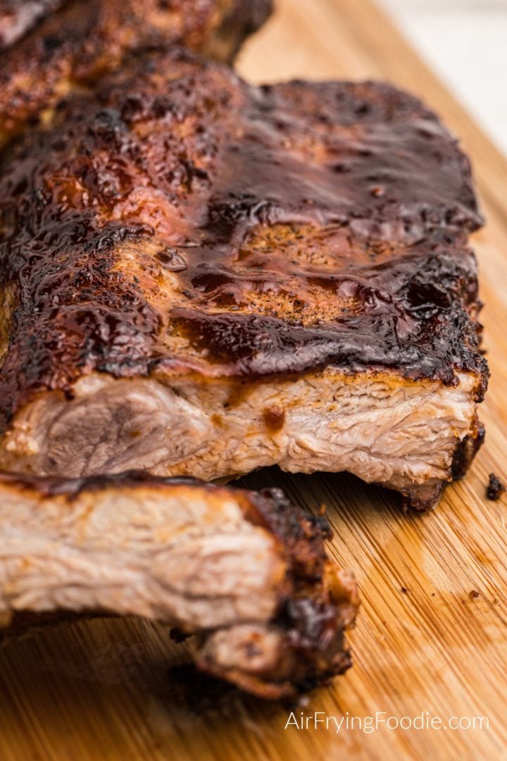 Air fryer ribs slathered in bbq sauce and sliced on a wooden cutting board. 