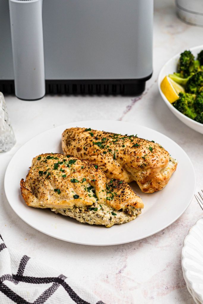 Golden seasoned stuffed chicken breasts on a white plate in front of an air fryer. 