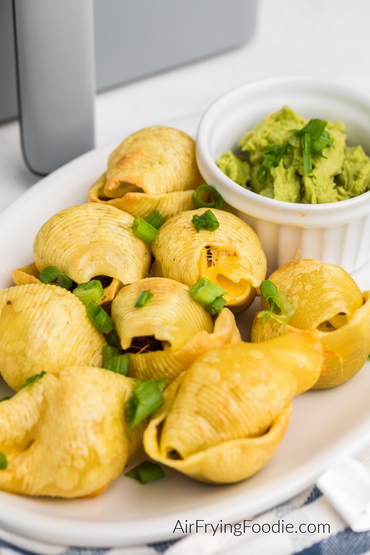 Taco stuffed shells made in the air fryer, served on a white plate with a side of guacamole.
