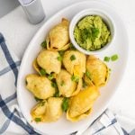 Taco stuffed shells on a plate topped with green onions and served with a side of guacamole.