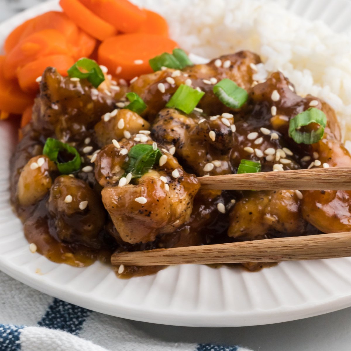 Air fryer teriyaki chicken on a plate with a side of rice and sliced carrots.