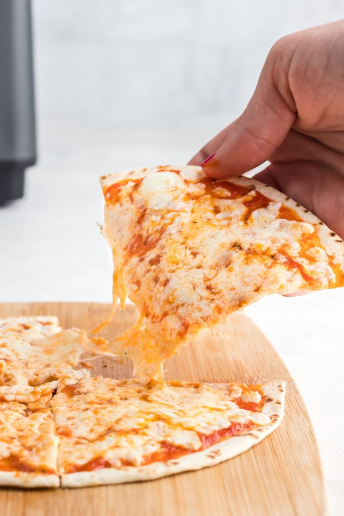 Cheesy tortilla pizza being pulled off of cutting board. 