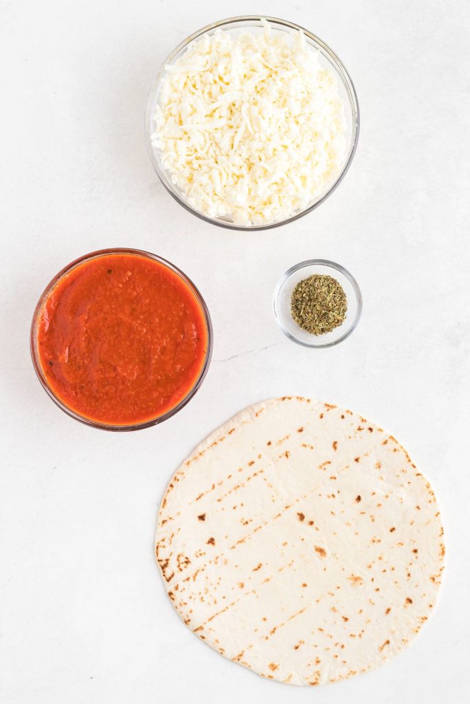 Shredded cheese, sauce, seasonings, and tortillas, on a white marble table. 