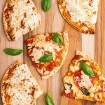Tortillas covered with melted cheese and pizza toppings on a wooden cutting board.
