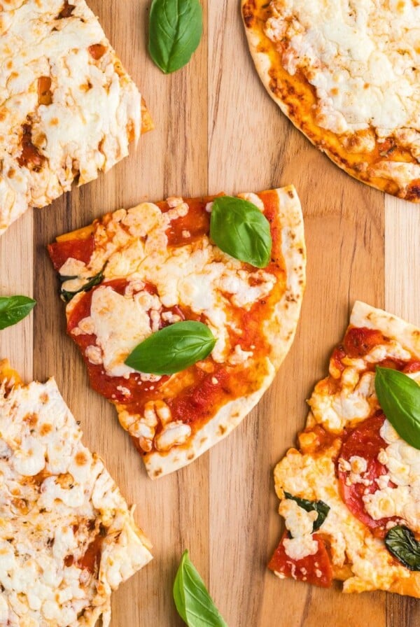 Tortillas covered with melted cheese and pizza toppings on a wooden cutting board.