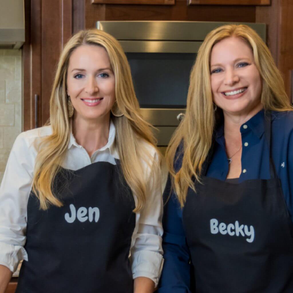 Jen and Becky, content creators and editors of air frying foodie, in the kitchen wearing aprons
