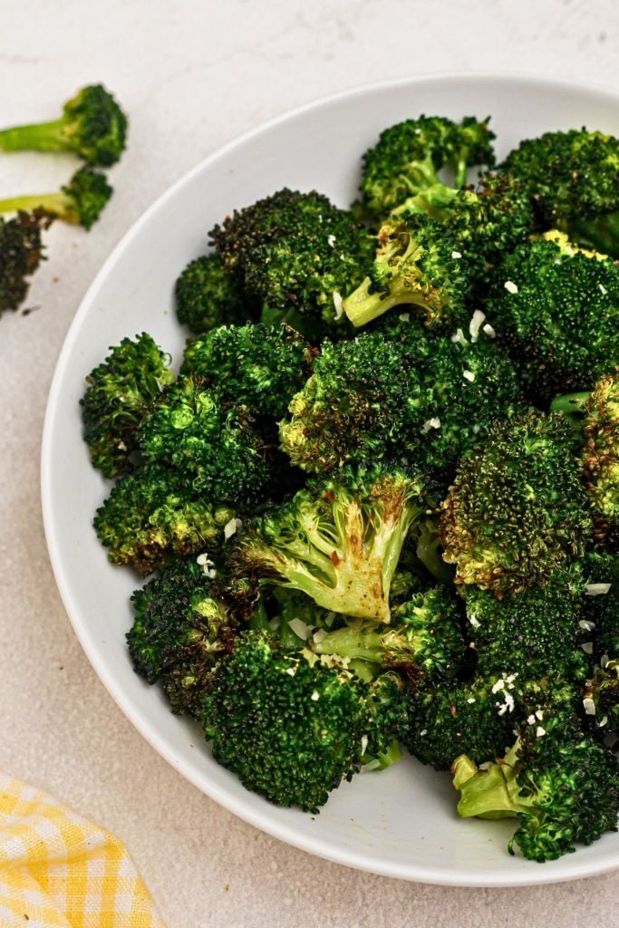 Green seasoned broccoli in a white bowl on a marble table. 