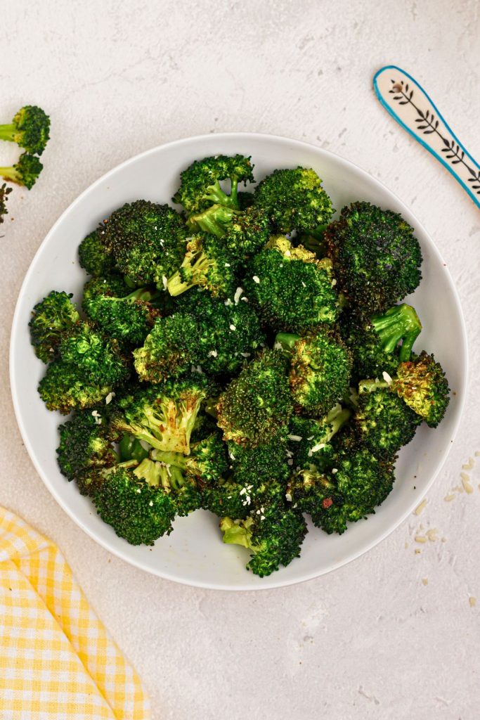 Bright green cooked broccoli in a white bowl sprinkled with seasonings and cheee. 