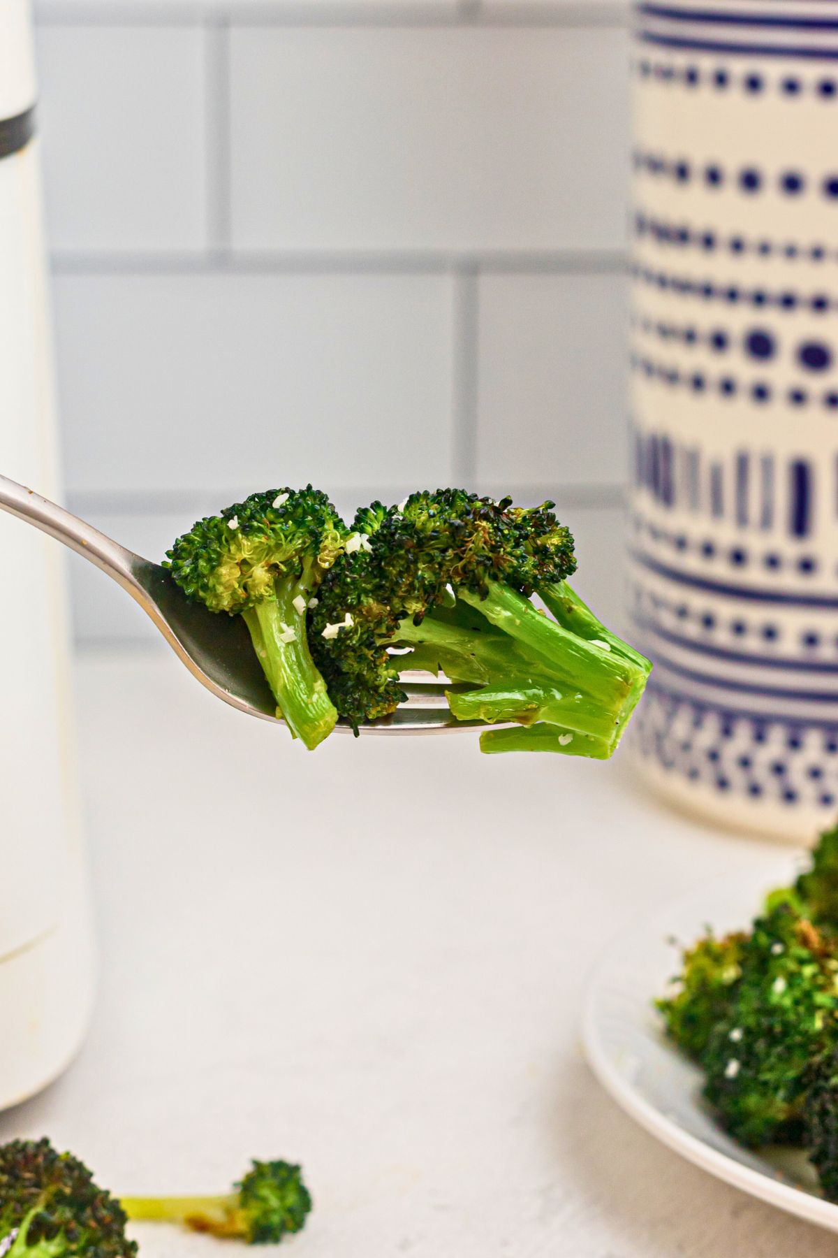 Air fryer broccoli florets on a fork in front of an air fryer.