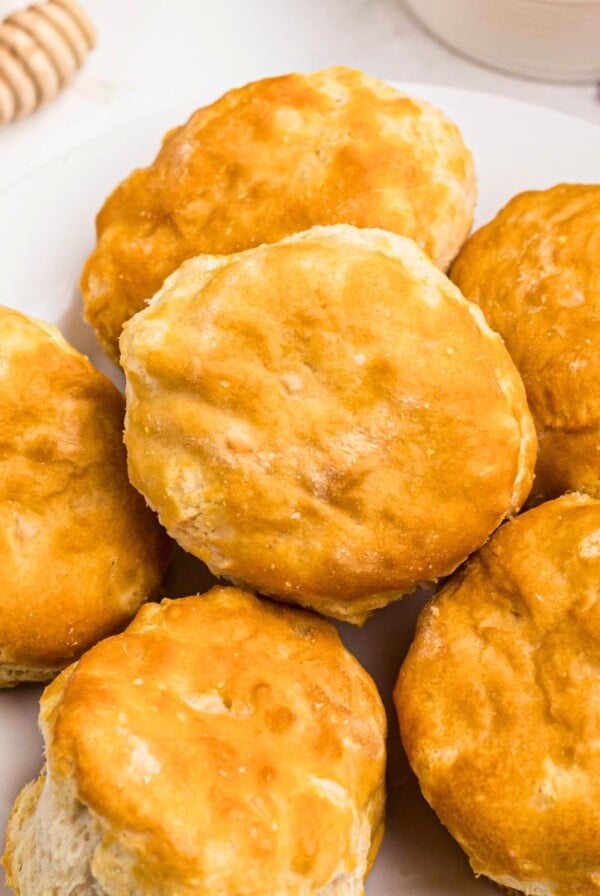 Golden biscuits on a white small plate in front of butter and honey.