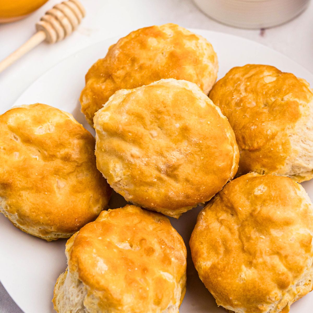 Golden biscuits on a white small plate in front of butter and honey.