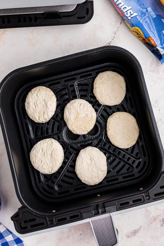 Frozen biscuits in the air fryer basket on a white marble table. 