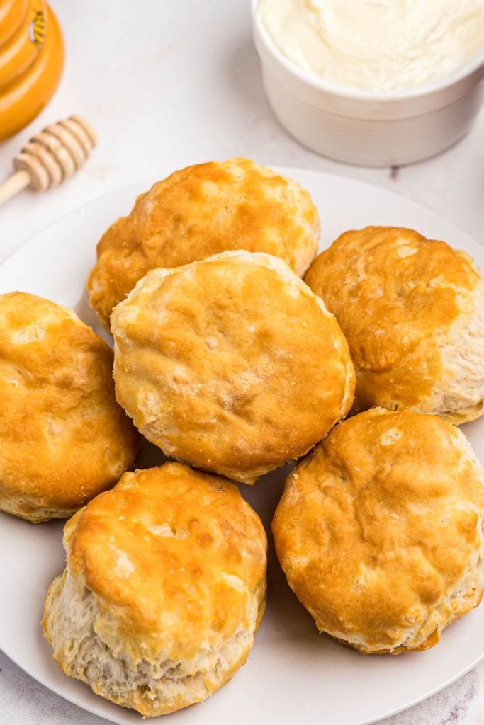 Golden fluffy biscuits on a small white plate with butter on the table. 