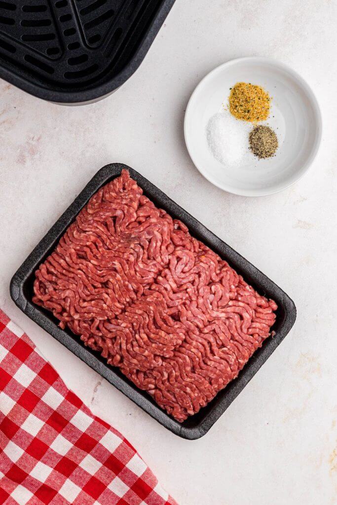 Ground beef with salt, pepper, and garlic powder, on a white marble table. 