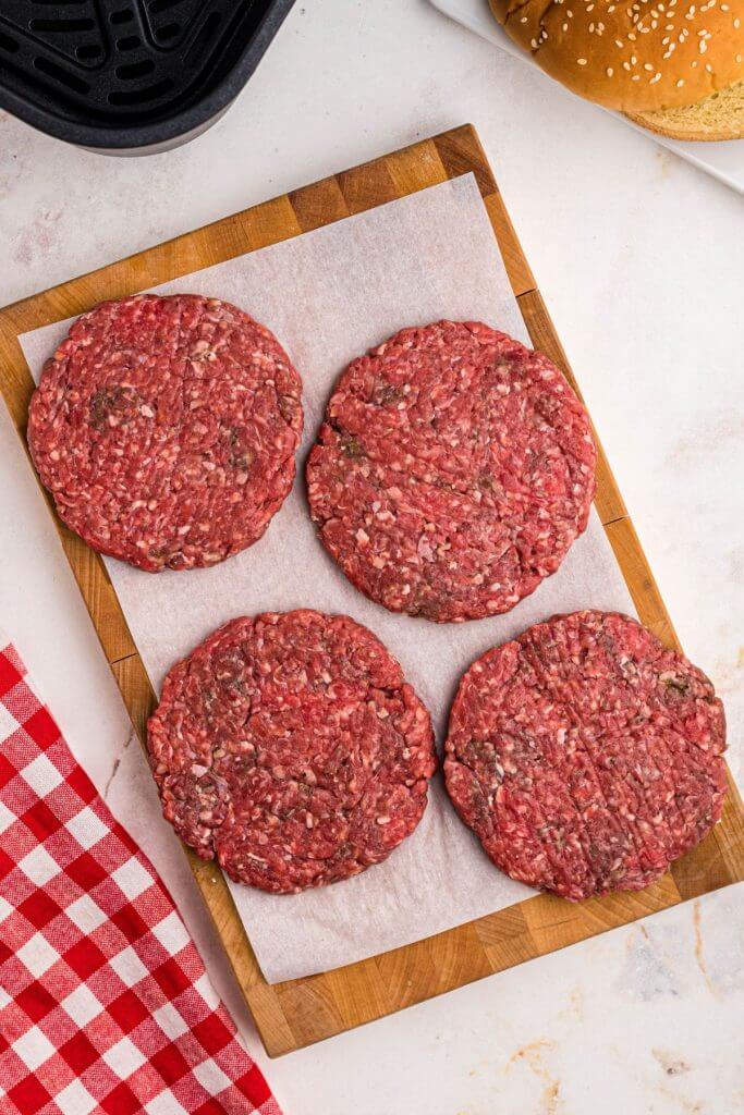 Ground beef shaped into four patties, on a wooden cutting board. 