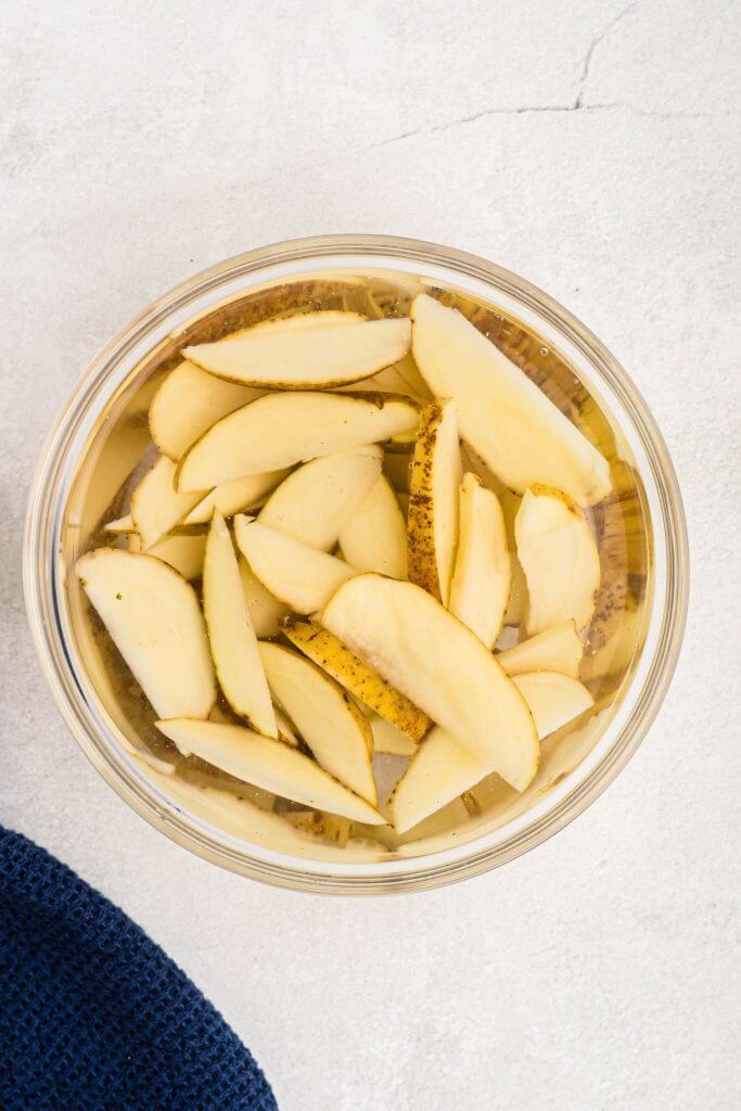 Clear glass bowl filled with ice water, with potato wedges soaking. 