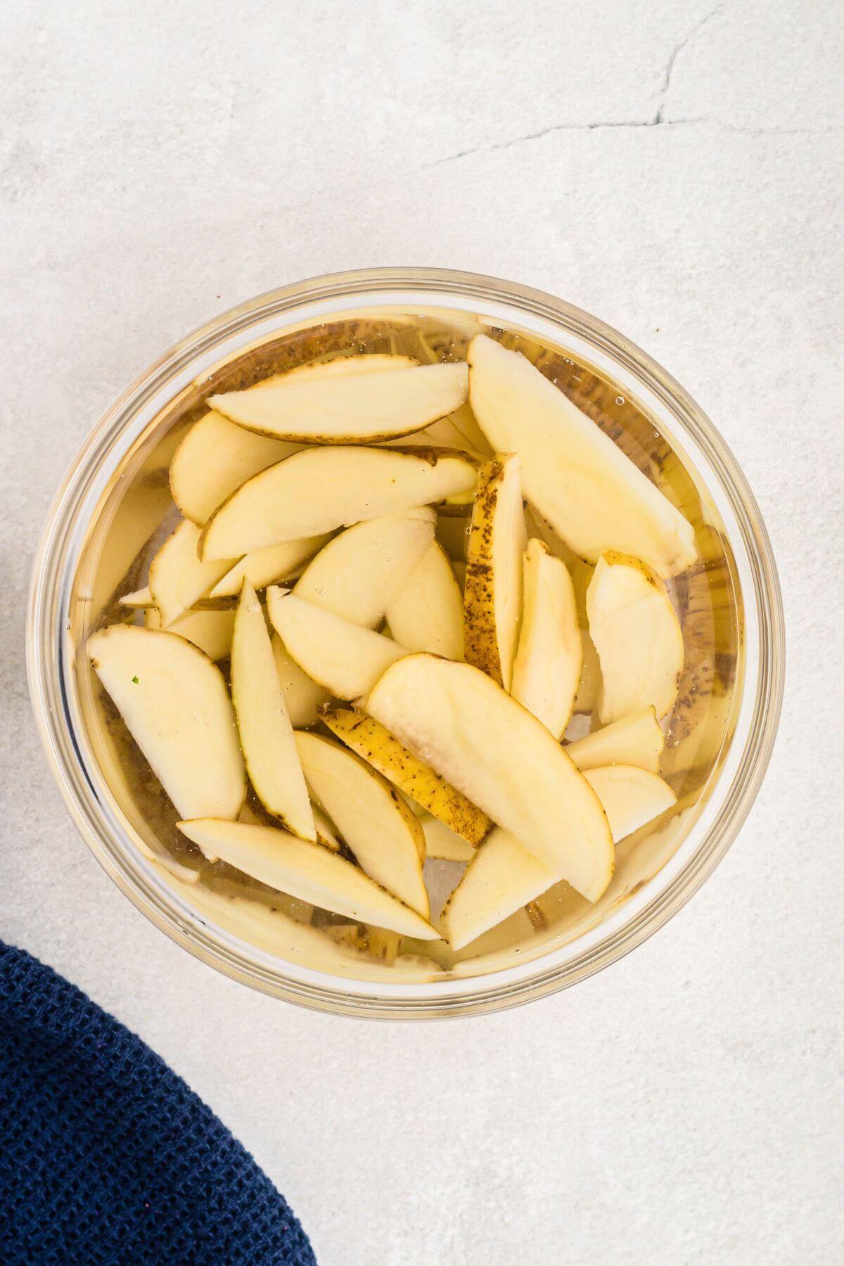 Clear glass bowl filled with ice water, with potato wedges soaking.