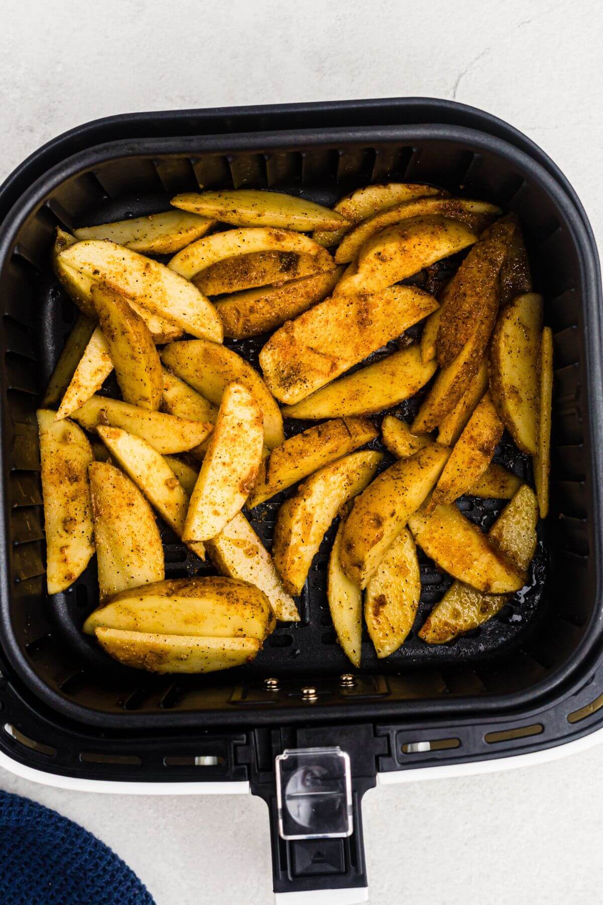 Uncooked potato wedges seasoned in an air fryer basket.