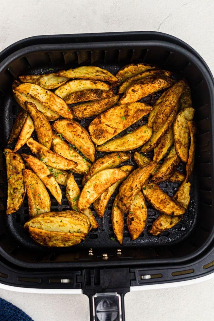Seasoned potato wedges in the air fryer basket after being cooked until golden. 