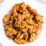 Golden crispy chicken pieces coated in an orange sauce served in a white bowl.