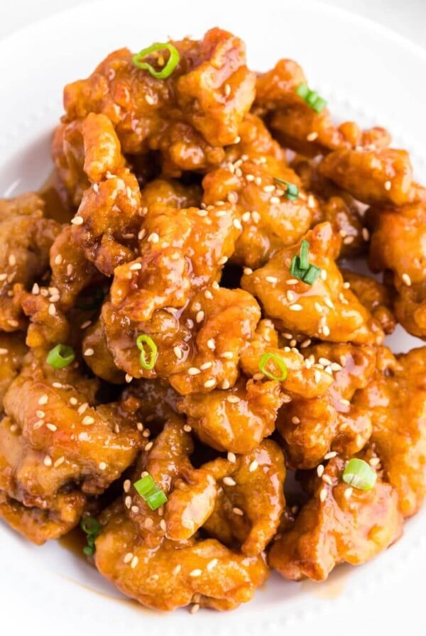 Golden crispy chicken pieces coated in an orange sauce served in a white bowl.