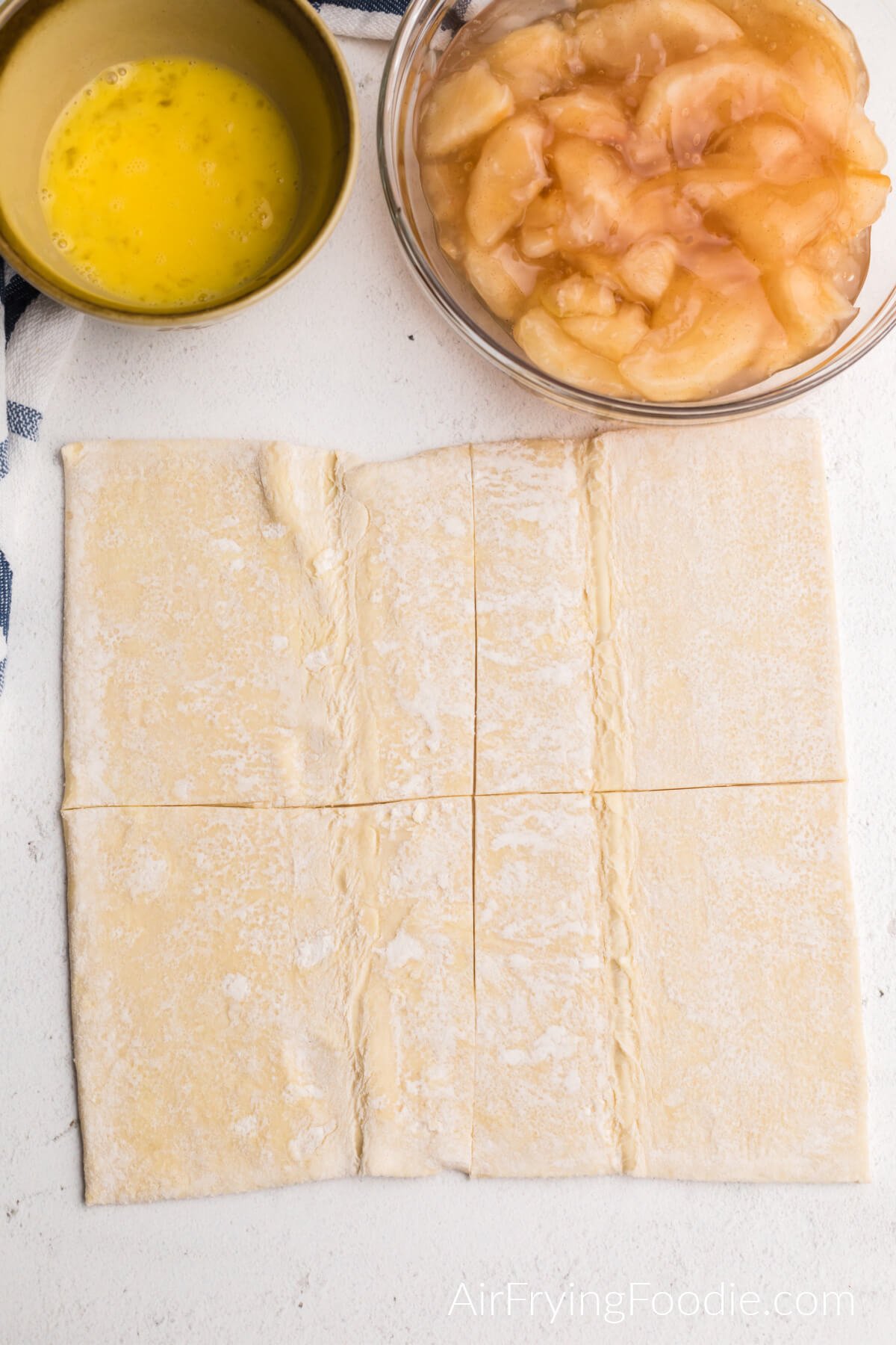 Puff pastry sheets cut into 4 squares, egg in a bowl, apple filling in a bowl. 