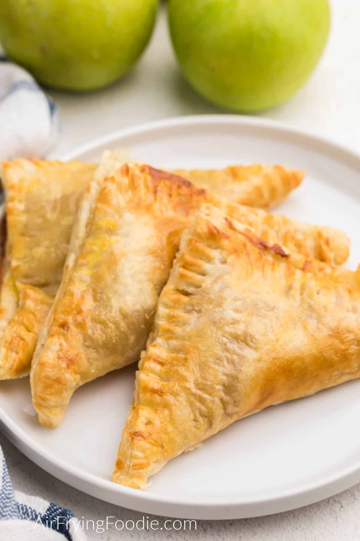 apple turnovers on a white plate with green apples in the background. 