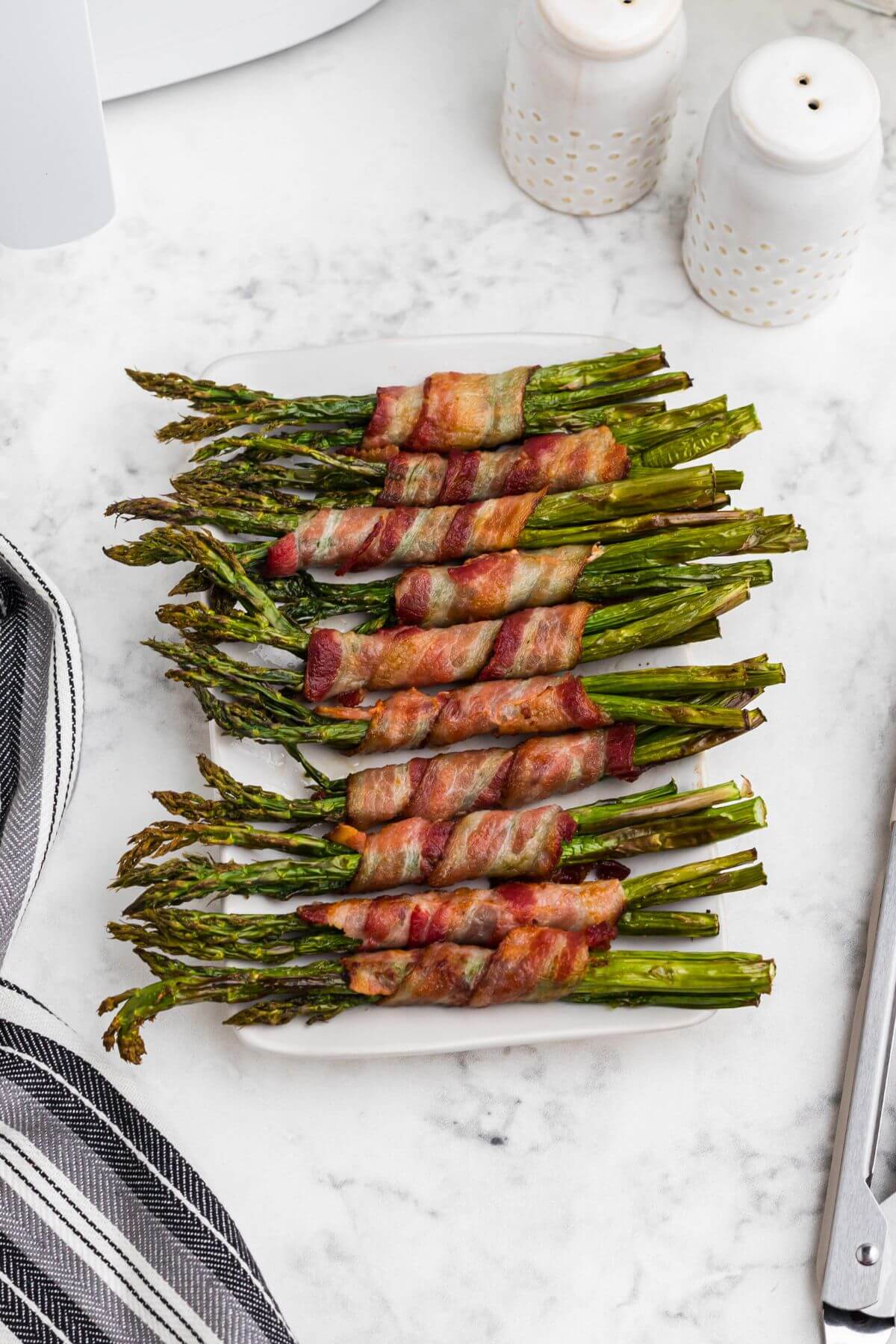 Crispy brown bacon wrapped around asparagus spears, on a white rectangle plate. 