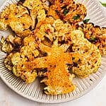 Golden cauliflower steaks on a small white plate after being cooked in the air fryer.