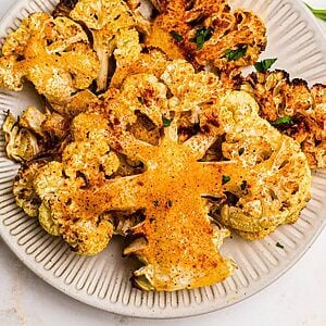Golden cauliflower steaks on a small white plate after being cooked in the air fryer.