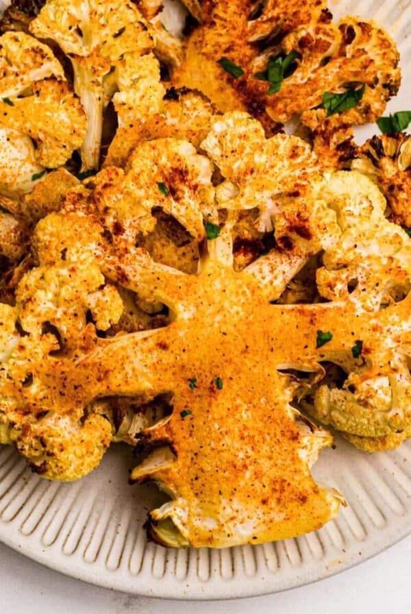 Golden cauliflower steaks on a small white plate after being cooked in the air fryer.